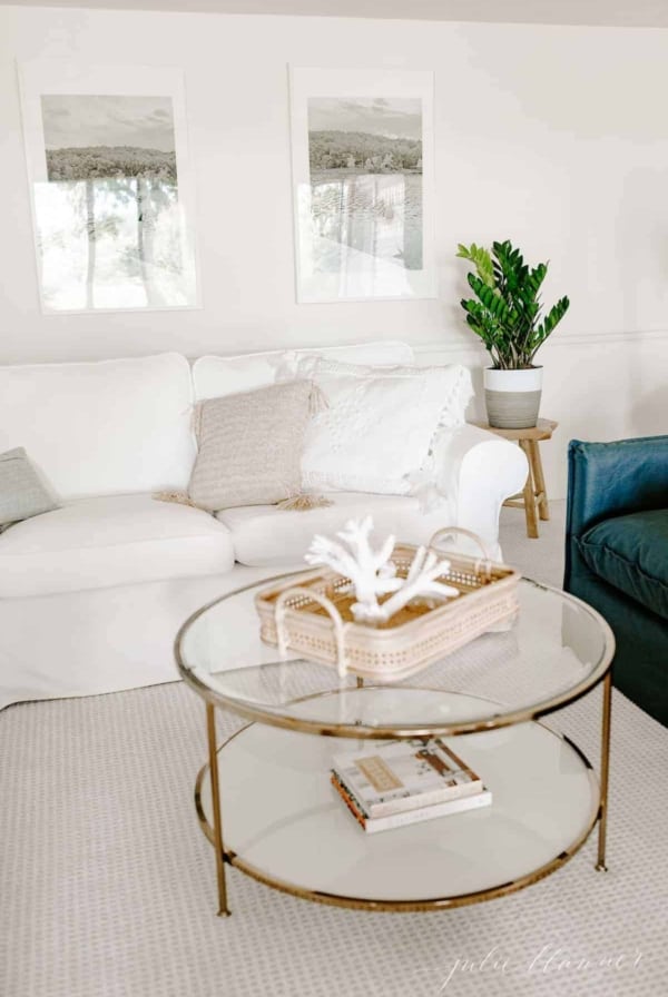 Living room scene with a white sectional, large photos on the wall and a wooden side table featuring a houseplant. #zzplant #zzplantcare