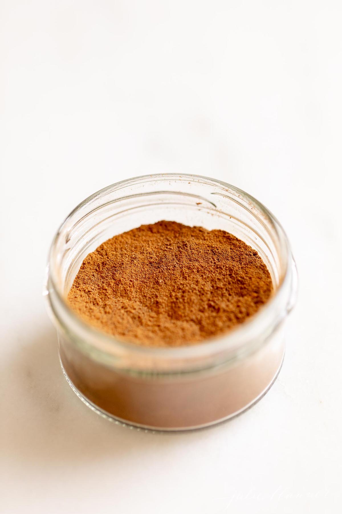 Homemade allspice blend in a small glass jar on a white countertop.