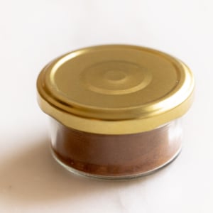 Homemade allspice blend in a small glass jar with a gold lid on a white countertop.