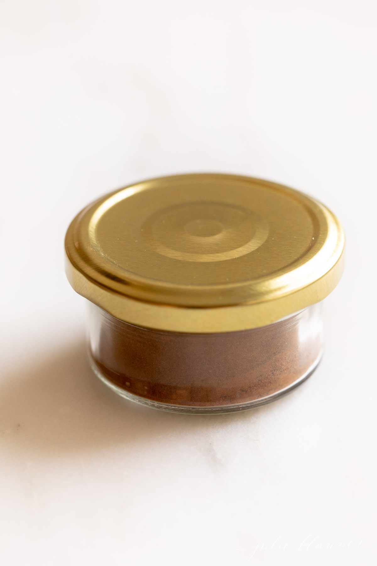 Homemade allspice blend in a small glass jar with a gold lid on a white countertop.