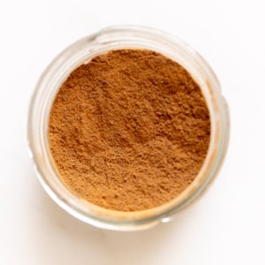 Homemade allspice blend in a small glass jar on a white countertop.