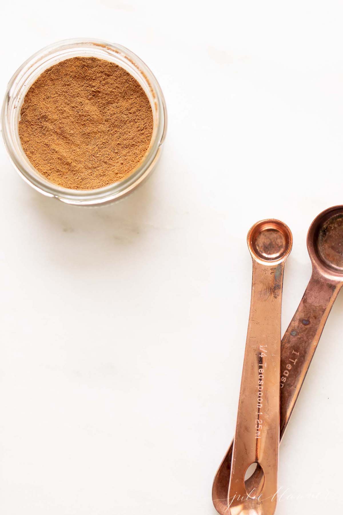 Allspice in a small glass container, measuring spoons to the side.