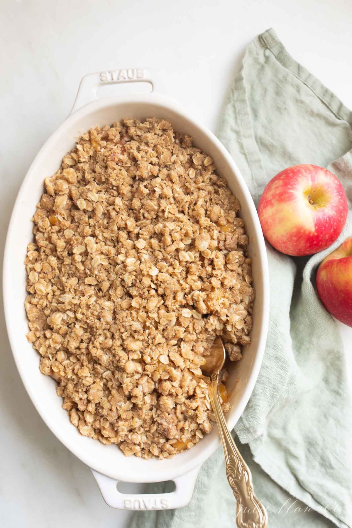 Apple crisp filling in a white oval baking dish with apples in the background