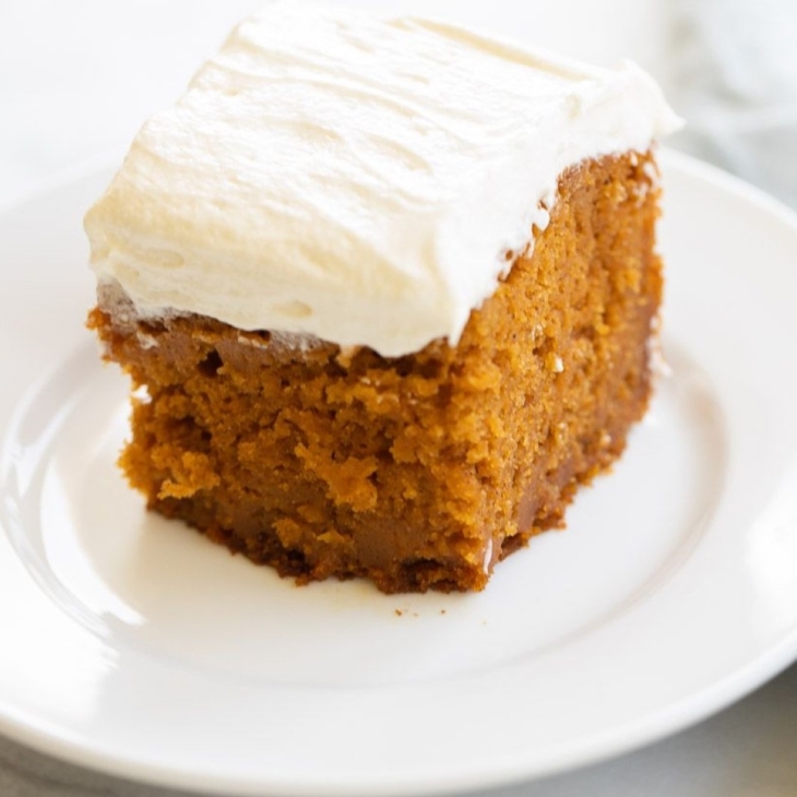 A slice of pumpkin cake with a thick layer of cream cheese frosting on a white plate.