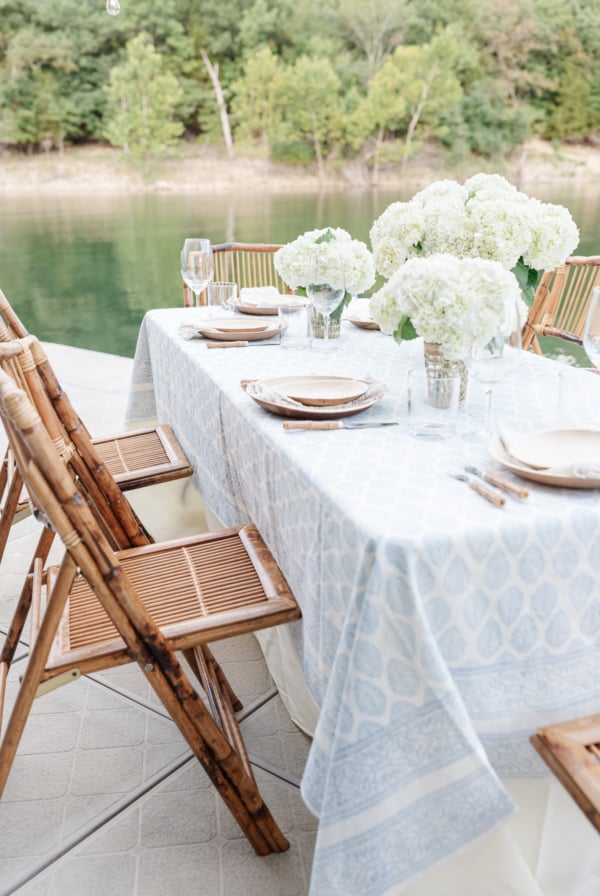 A blue and white block print table setting on a wooden deck next to a lake.