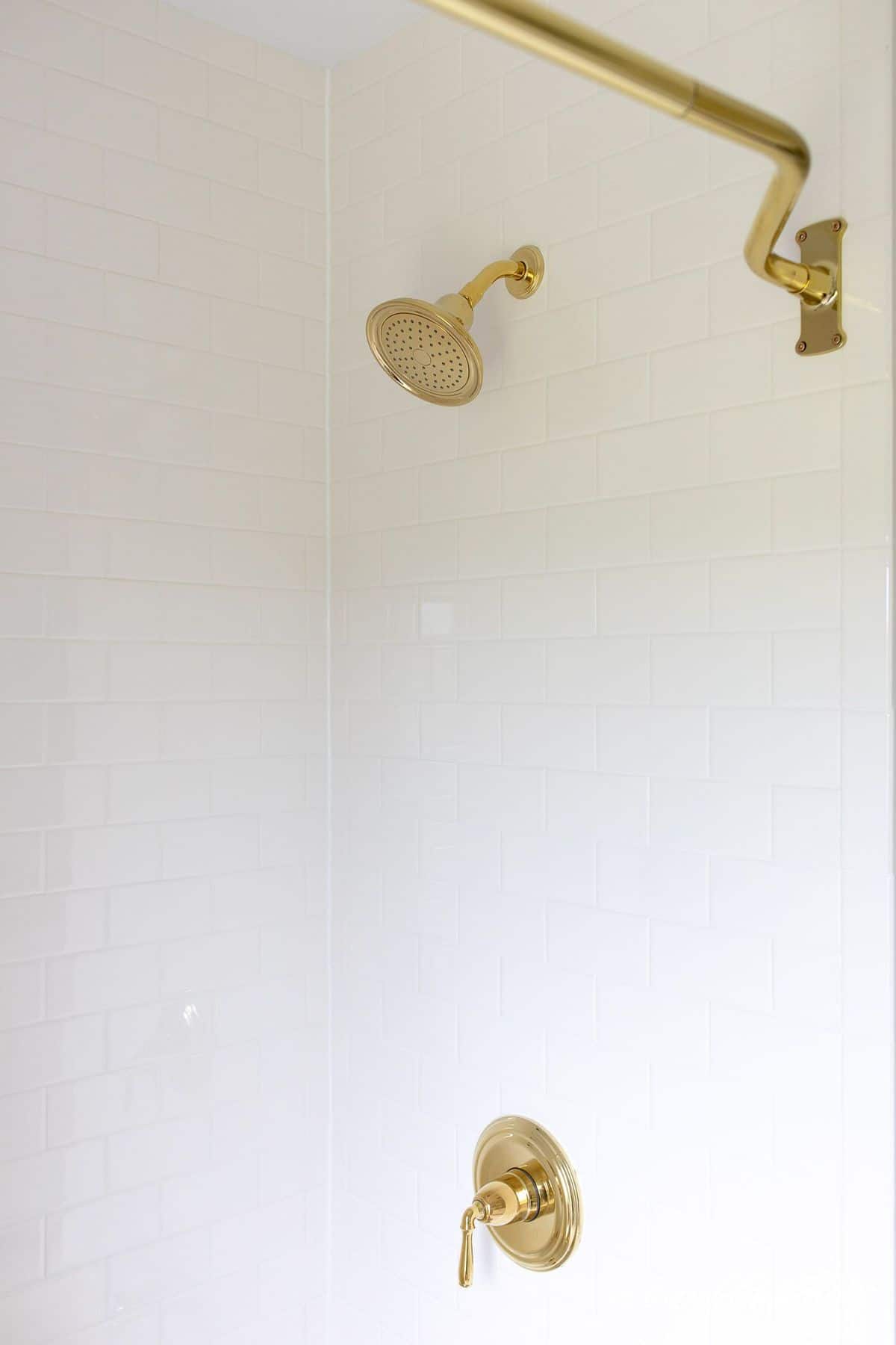 White subway tile shower with brass showerhead and bathtub fixtures. 