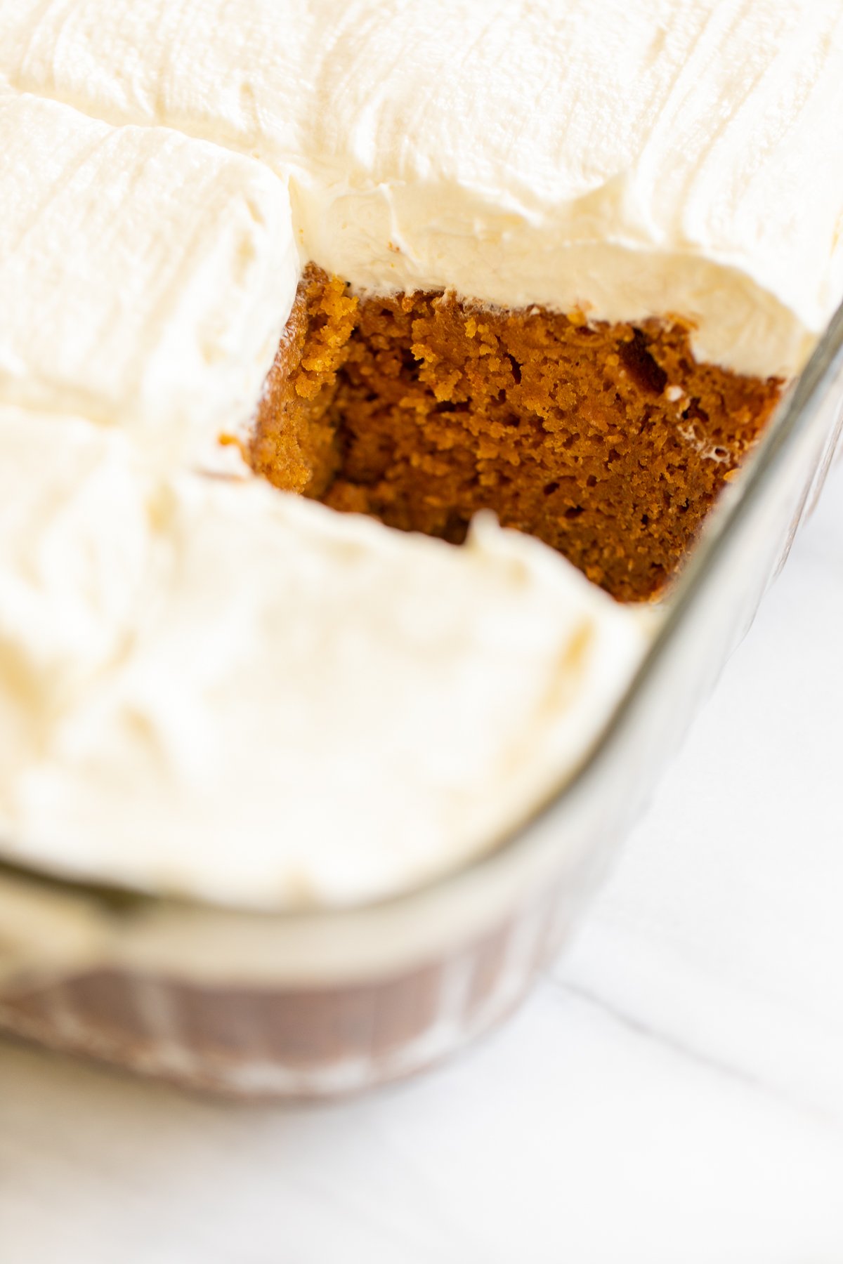 A slice of pumpkin cake with cream cheese frosting in a glass dish.