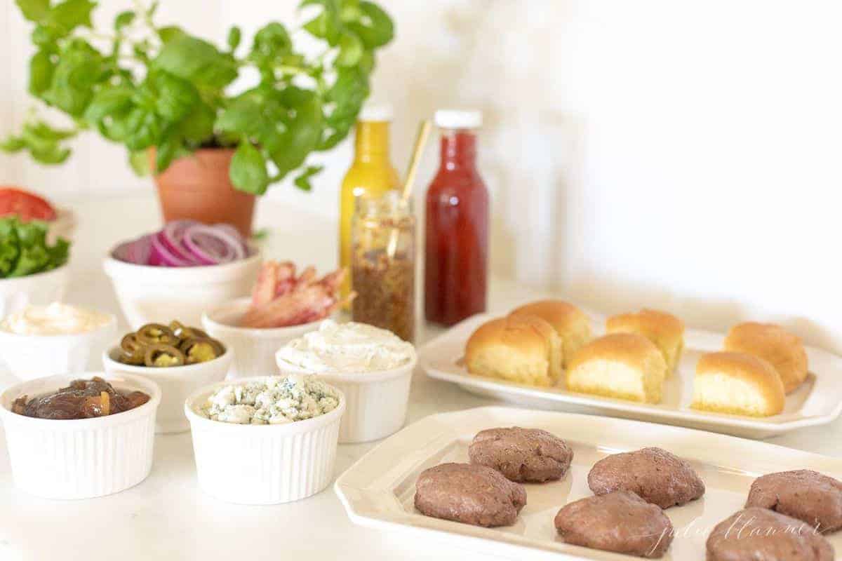 Burger toppings displayed in white ceramic bowls, slider in foreground. #burgerbar #burgershop #sliderbar