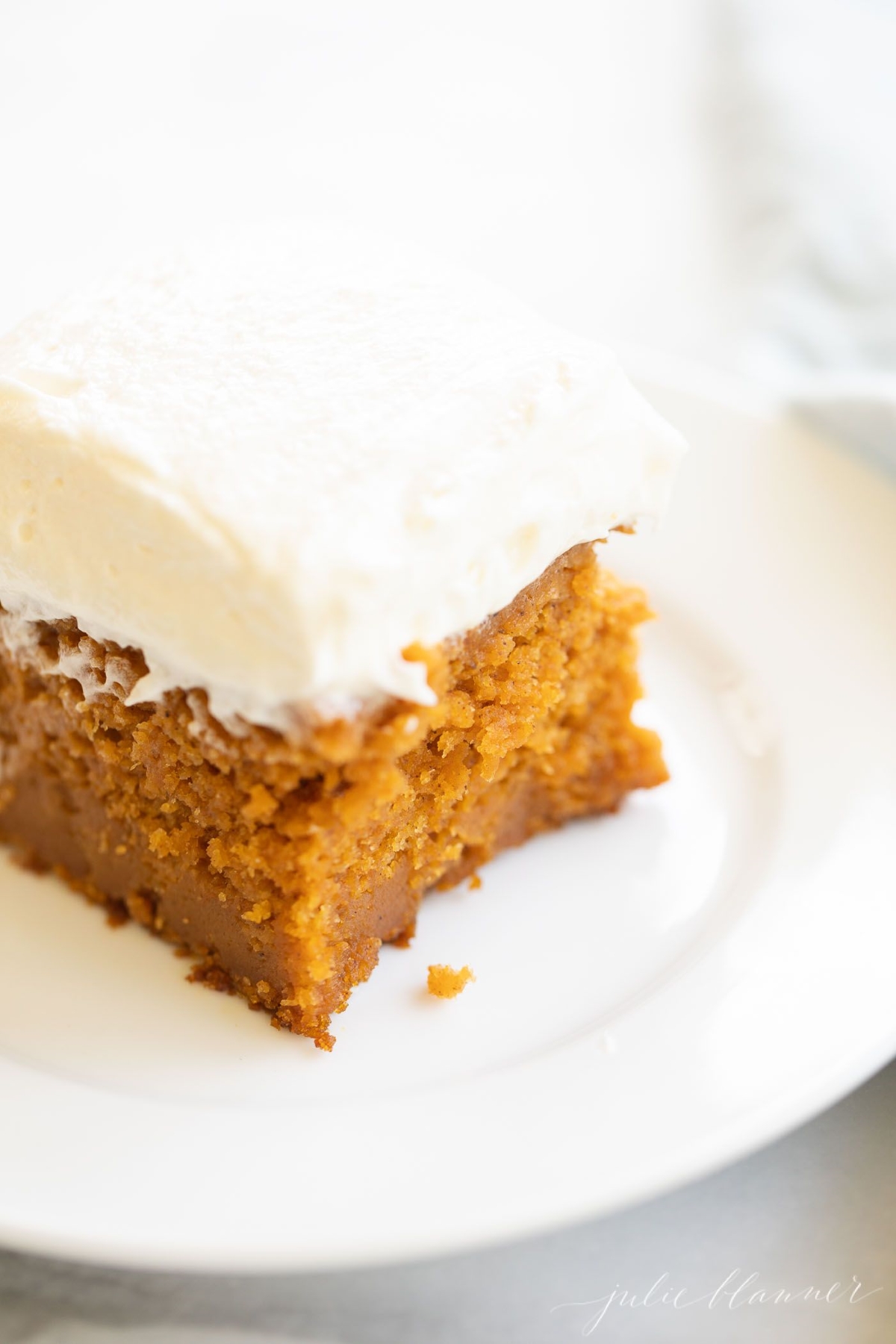 A slice of pumpkin cake with a thick layer of cream cheese frosting on a white plate.