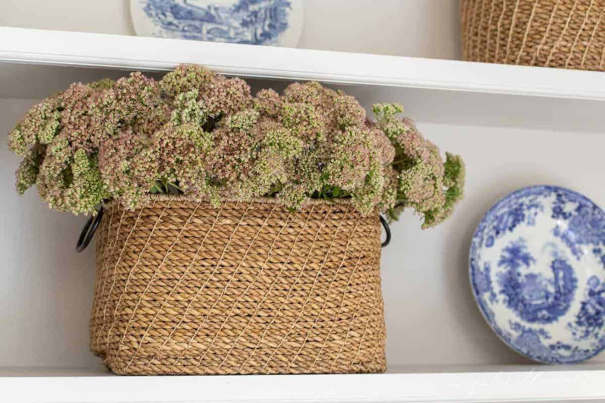 Large basket place on bookshelf, filled with fresh flowers. #falldecor