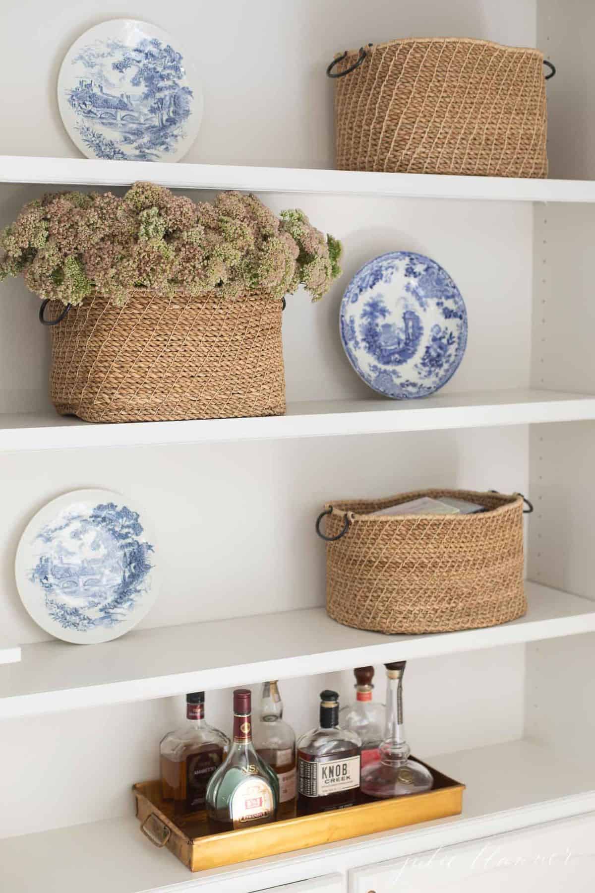 Built in book shelves with a tray of liquor, basket of flowers and blue and white plates. #falllivingroom