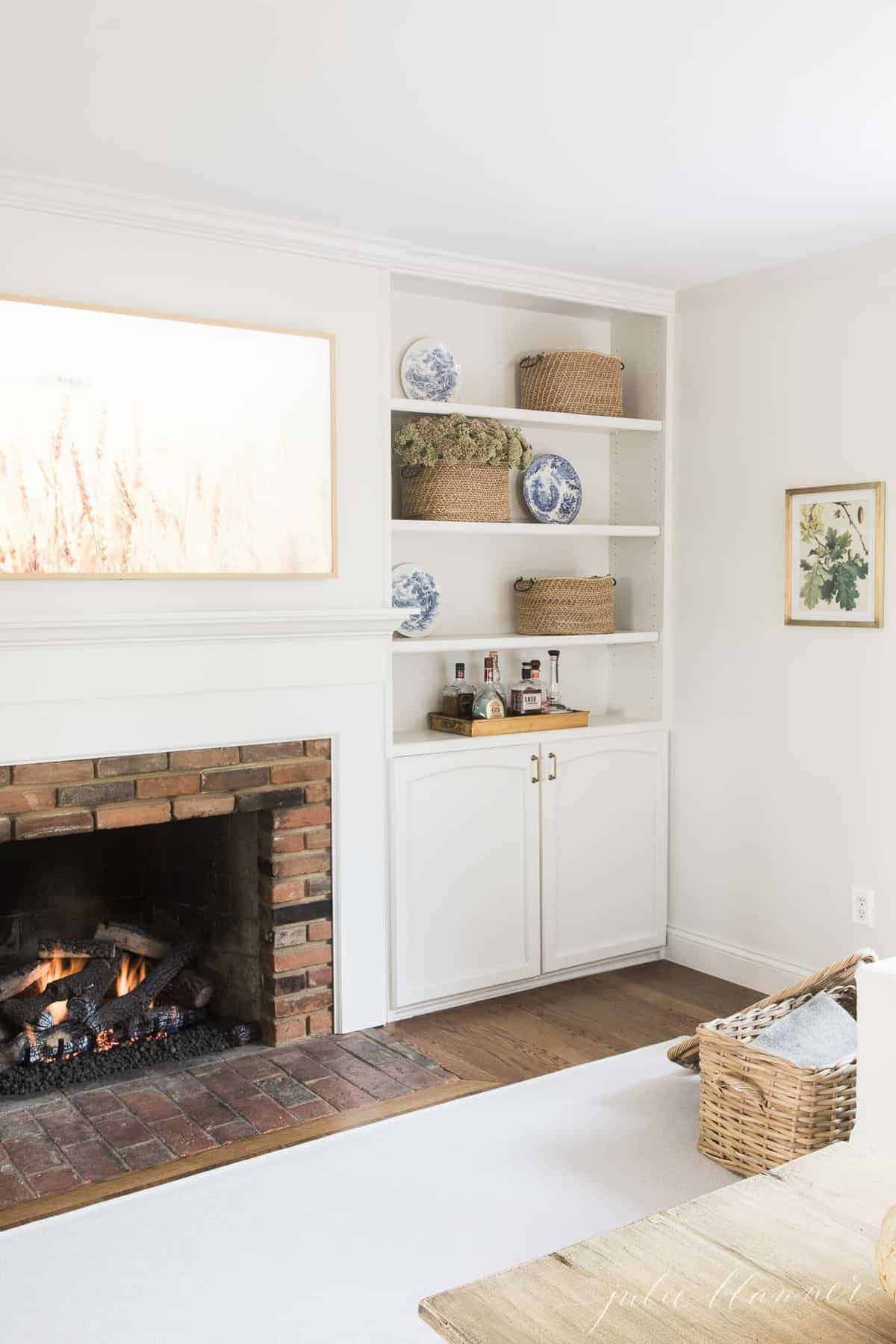 Living room fireplace burning with artwork above and bookshelves on the side. #falllivingroom