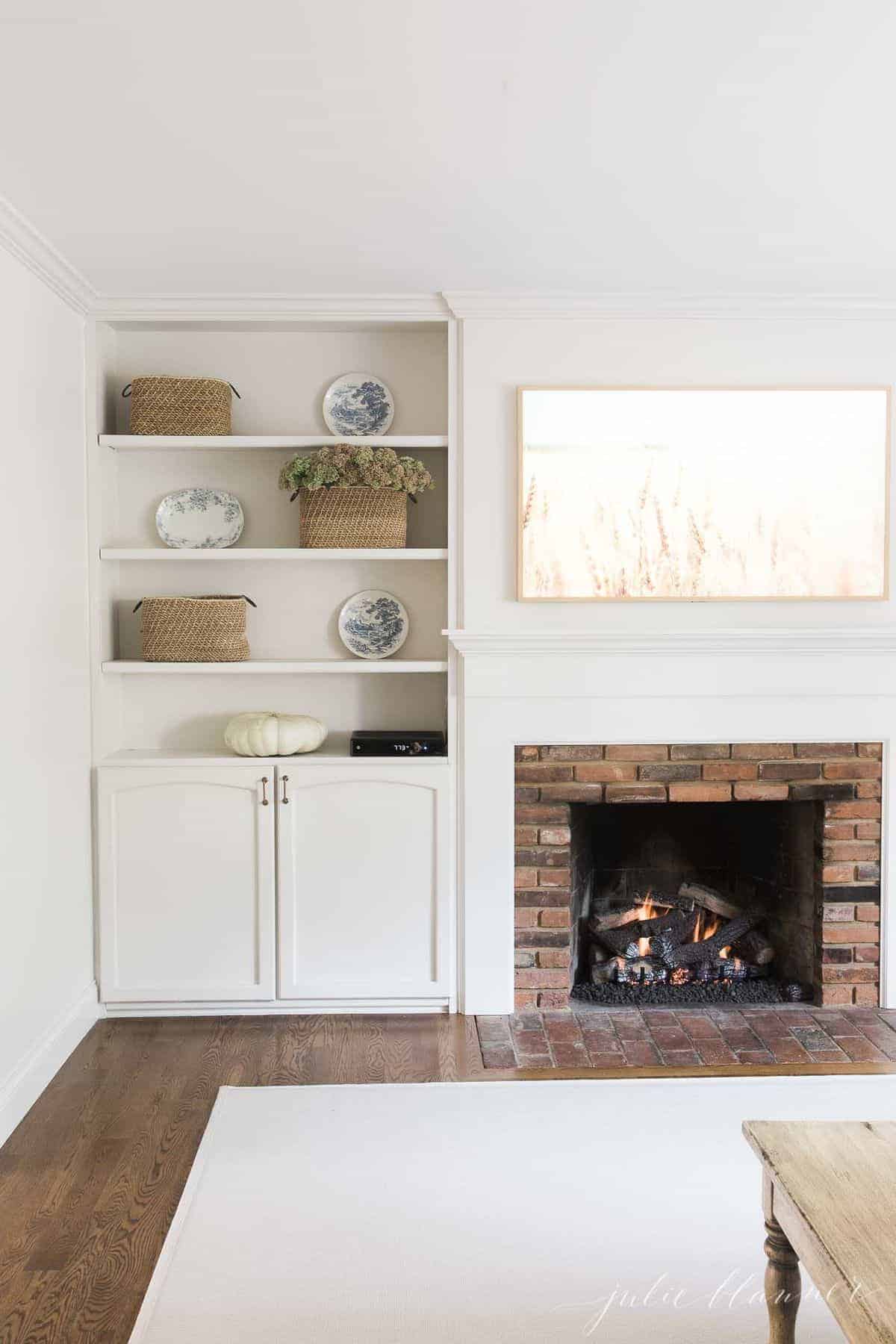 Living room fireplace burning with artwork above and bookshelves on the side. #falllivingroom