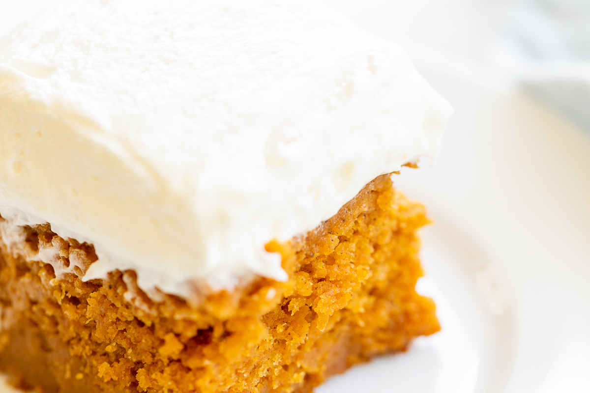 A slice of pumpkin cake with cream cheese frosting on a white plate.