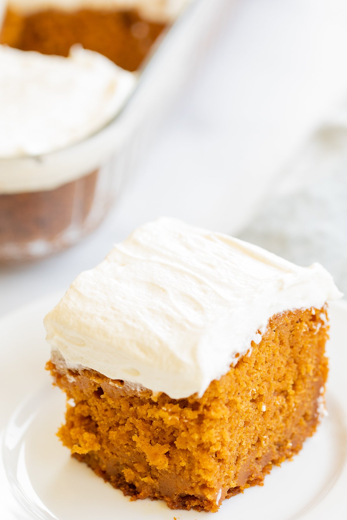 A slice of pumpkin cake topped with cream cheese frosting on a white plate.