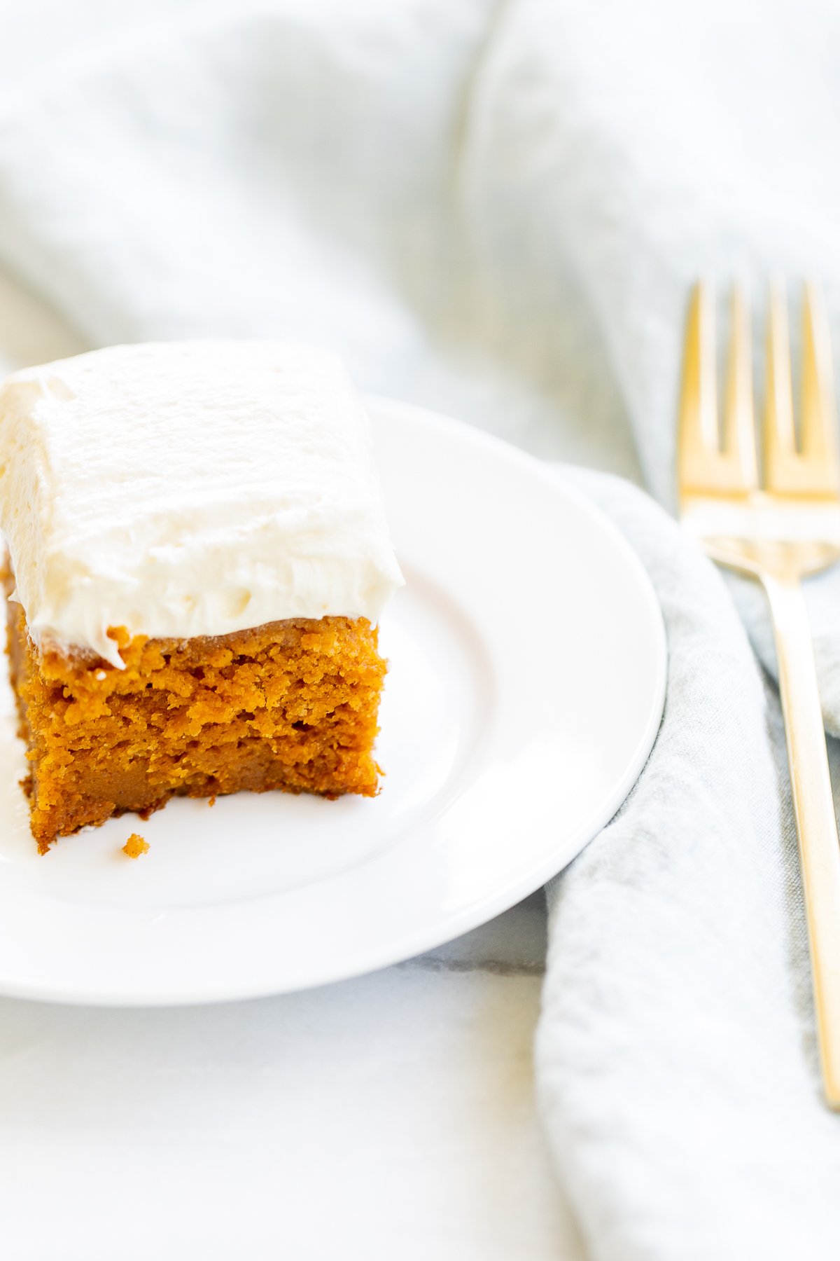 A slice of pumpkin cake with fluffy cream cheese frosting on a plate.