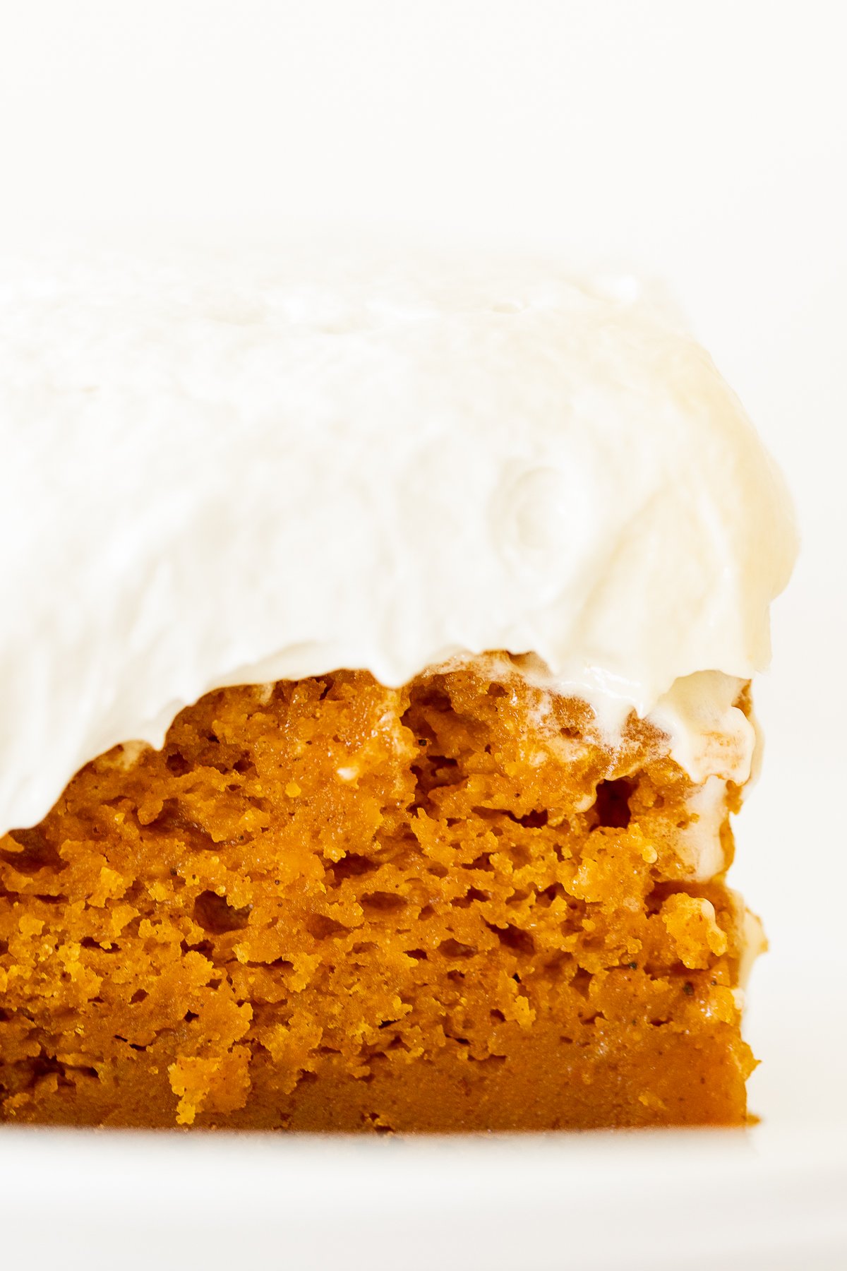 A slice of pumpkin cake with fluffy cream cheese frosting on a white plate.