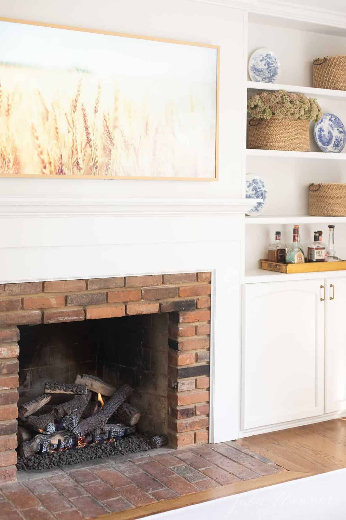 Living room fireplace burning with artwork above and bookshelves on the side. #falllivingroom