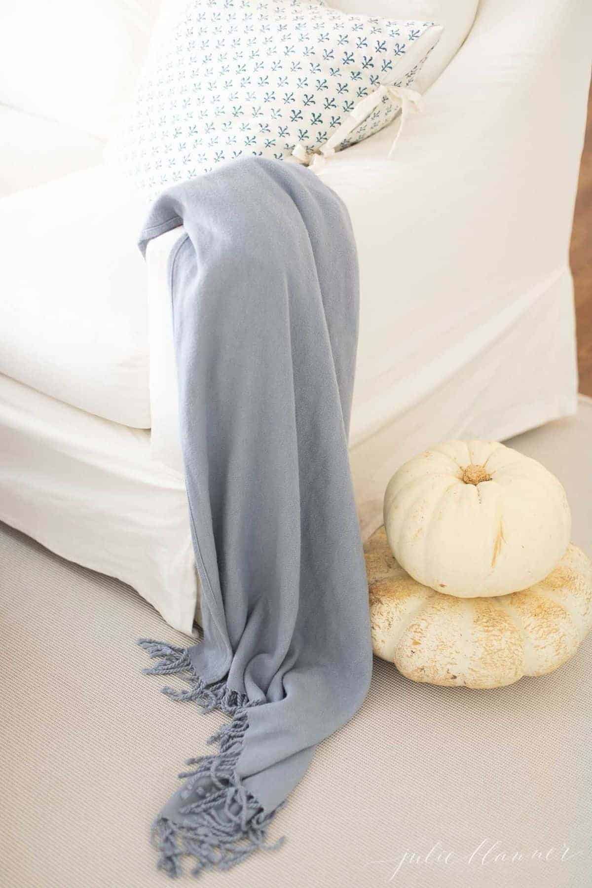 Looking down on corner of white sofa, soft blue throw over the arm. Stack of white heirloom pumpkins to the side. #falllivingroom