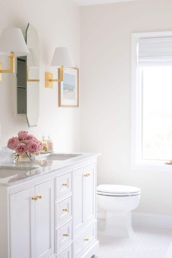 White bathroom with gold touches, mirrored medicine cabinet is slightly ajar. #spabath