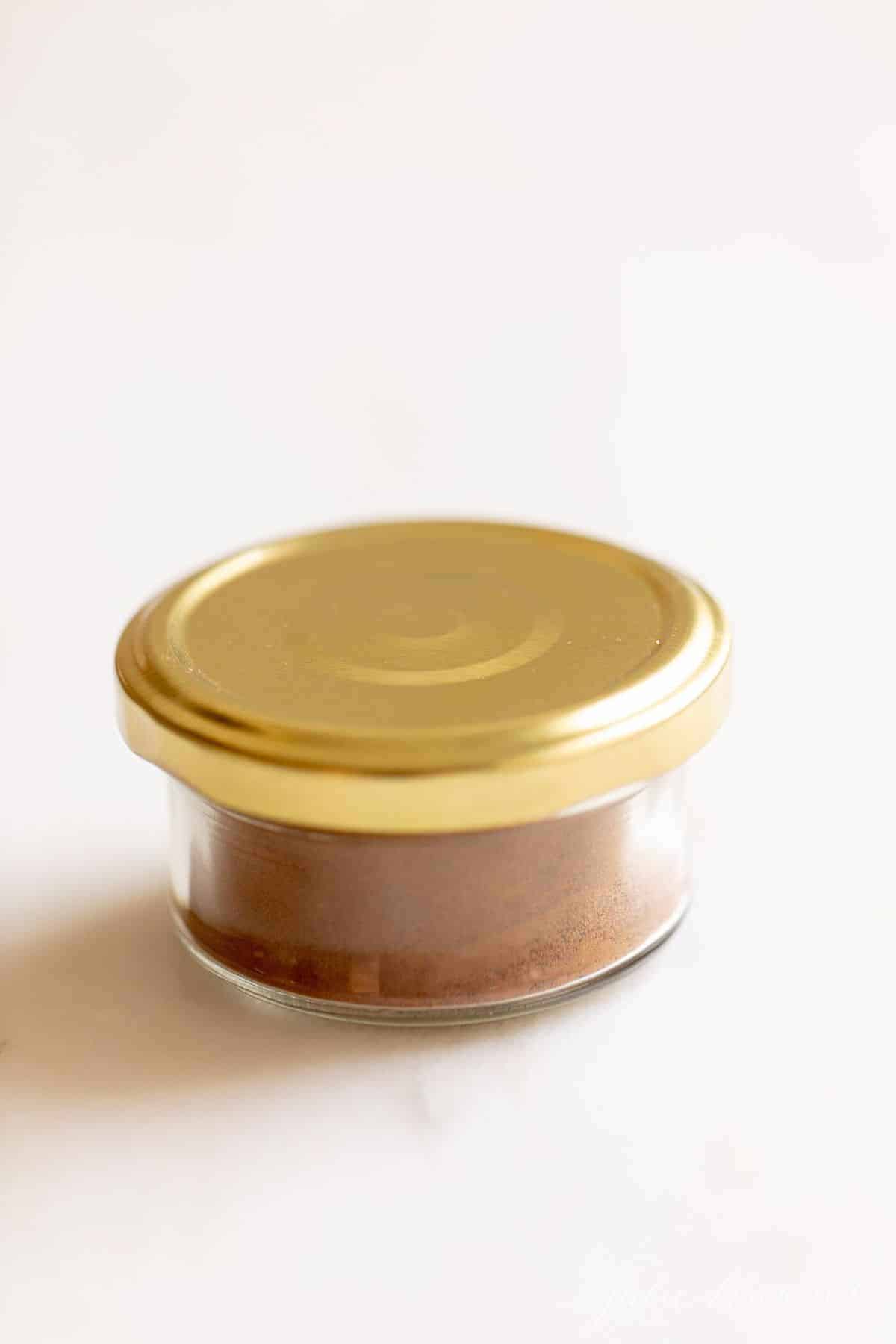 Clear jar of spices with a gold lid, on a white counter top.