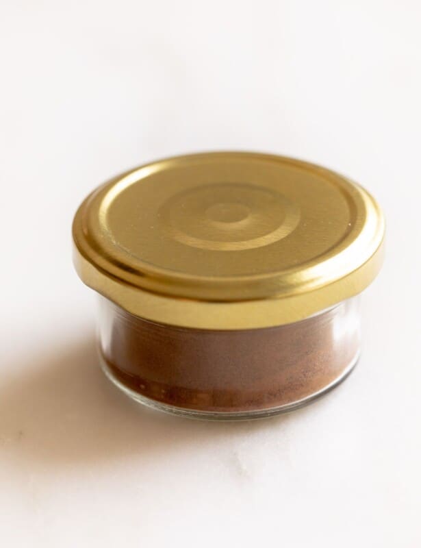 Clear jar of spices with a gold lid, on a white counter top.