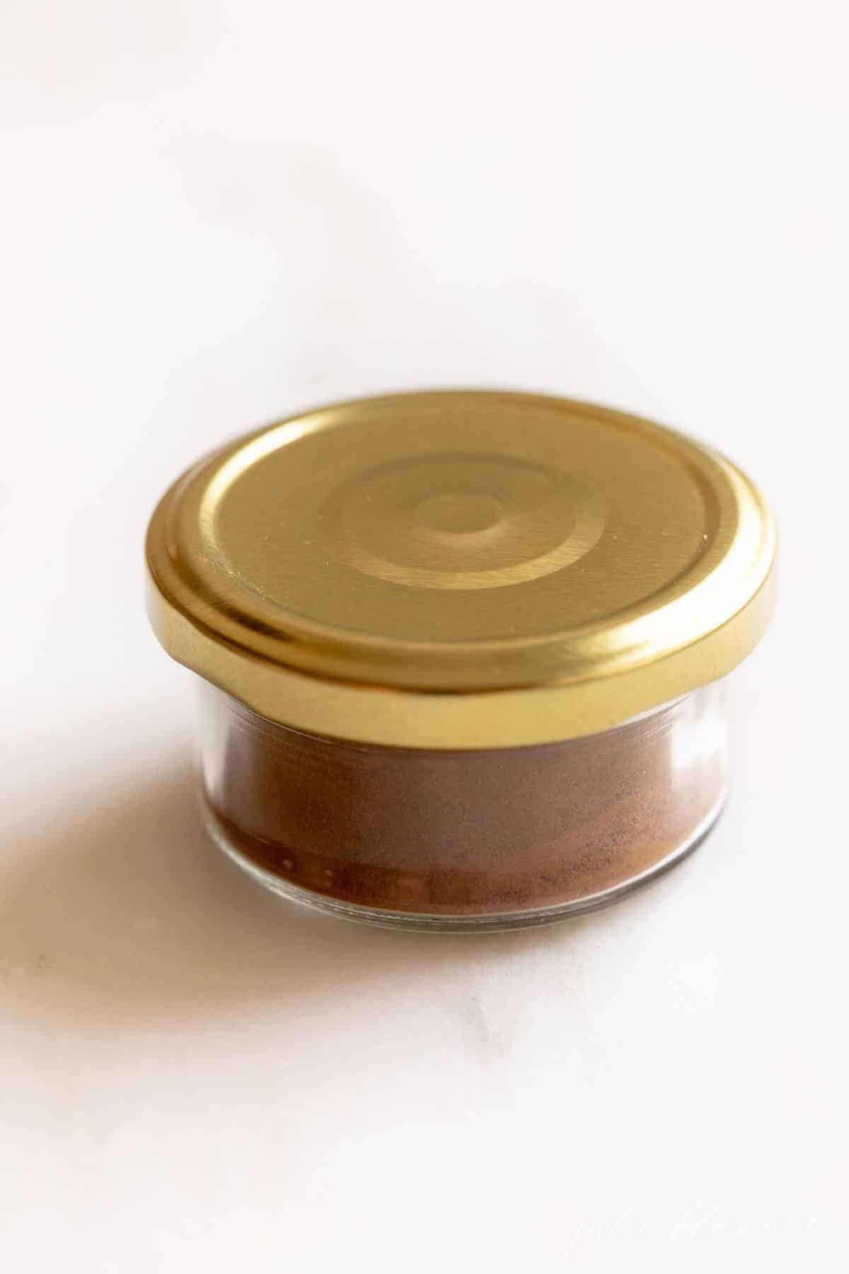 Clear jar of spices with a gold lid, on a white counter top.