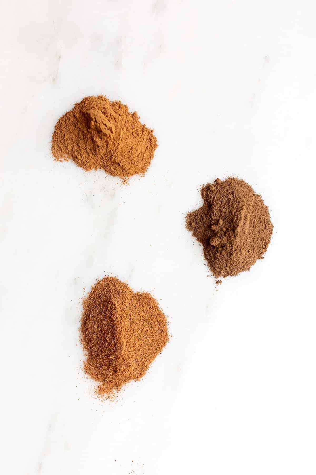 Three small piles of spices on a white marble counter top. 