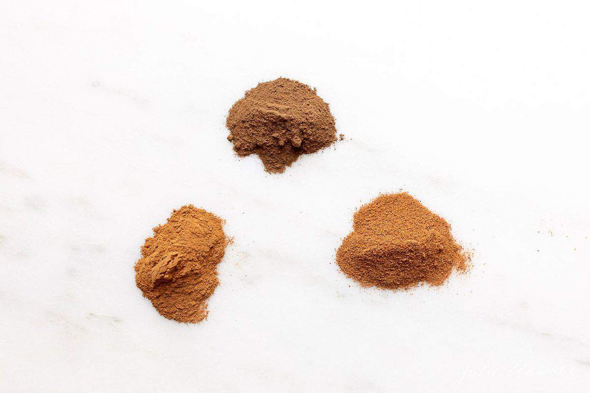 Three small piles of spices on a white marble counter top. 