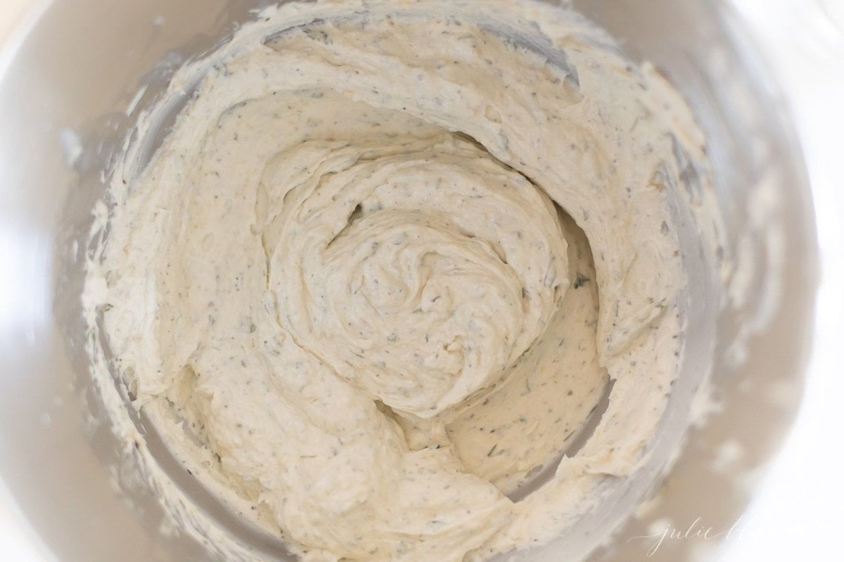 A mixing bowl full of herbed cream cheese for a homemade Boursin cheese recipe.