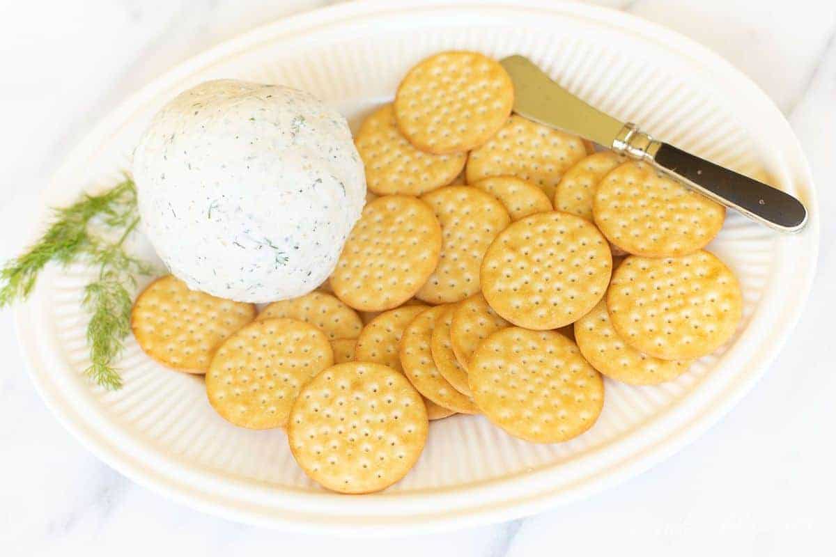 Boursin cheese ball on a white platter with crackers around it. 