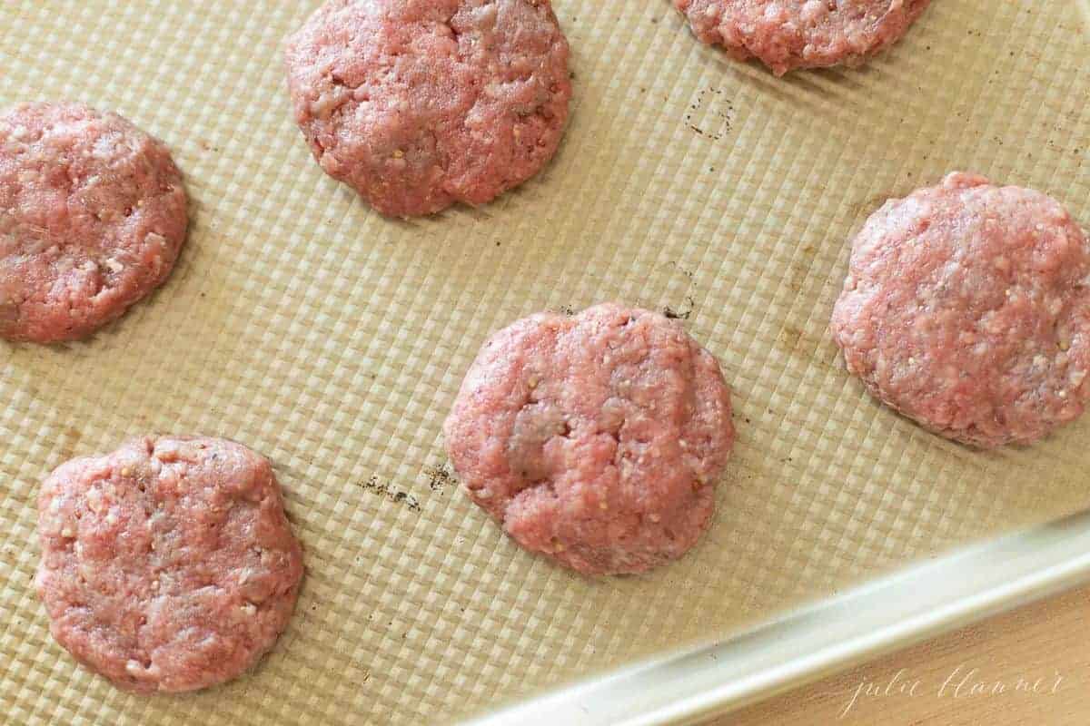 Six raw burger patties on a gold baking sheet waiting to go into oven. 