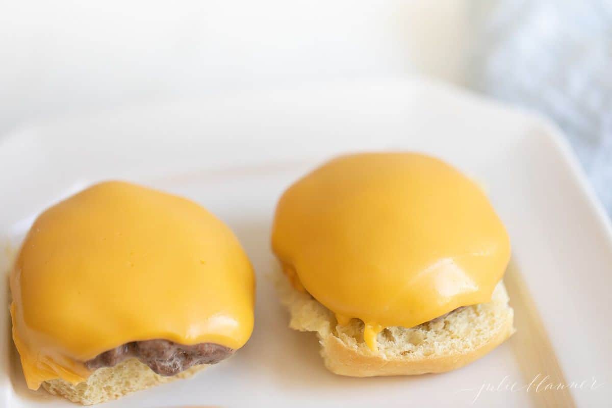 Cheeseburger sliders on a white surface without the top bun. 