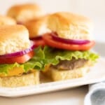 Burgers stacked with lettuce, tomato and onion on a white platter. #burgersintheoven