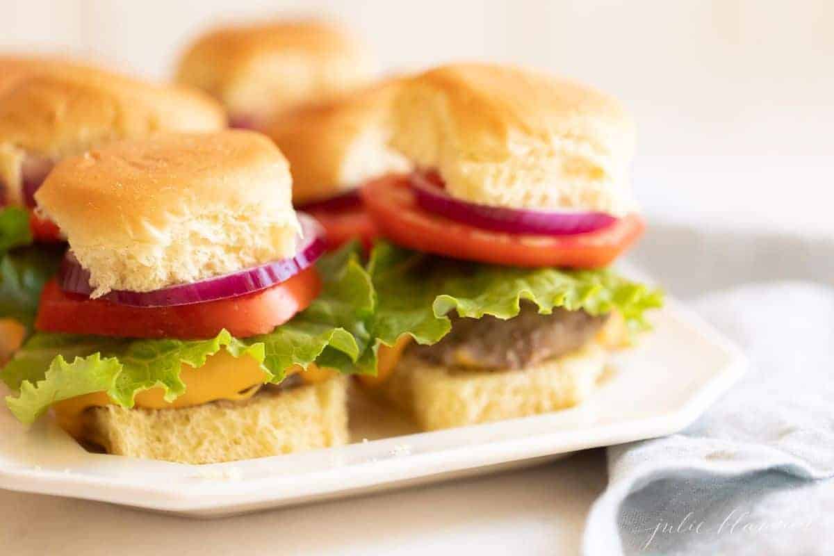 Burgers stacked with lettuce, tomato and onion on a white platter. #burgersintheoven