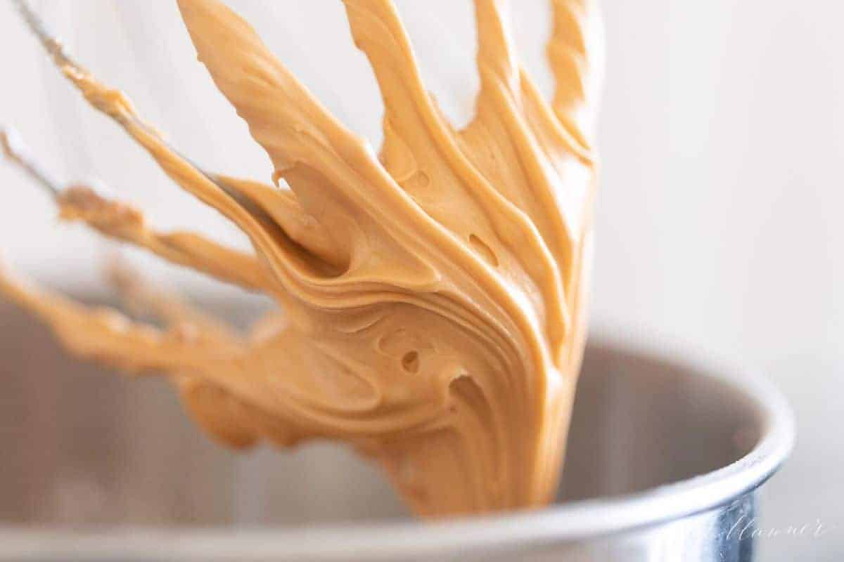 Butterscotch frosting on a metal mixer attachment, edge of metal bowl showing at bottom.