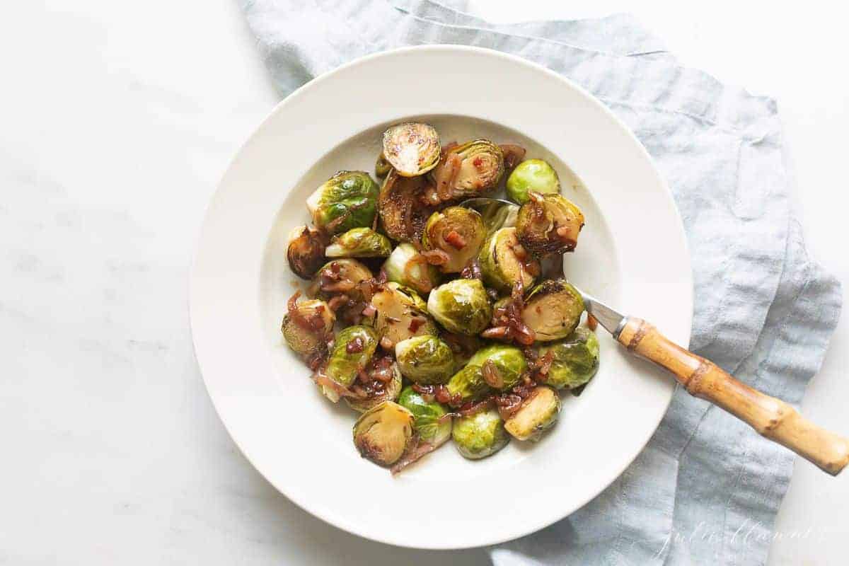 White bowl with sauteed brussel sprouts, blue linen napkin to the side.