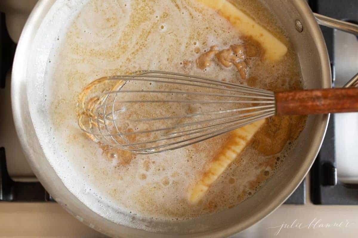 Whisk that is combining melted peanut butter and butter in a saucepan.