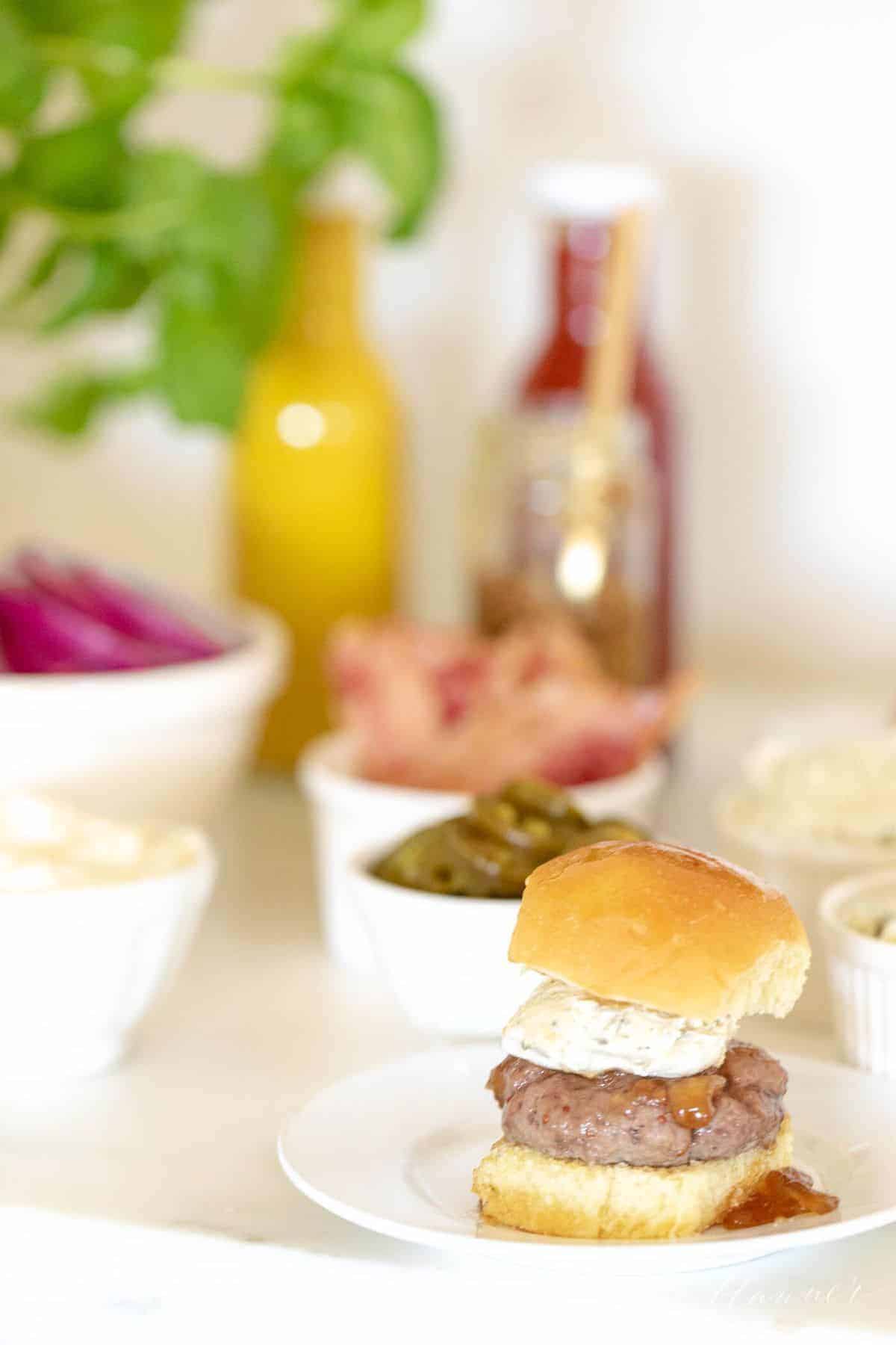 Burger toppings displayed in white ceramic bowls, slider in foreground. #burgerbar #burgershop #sliderbar