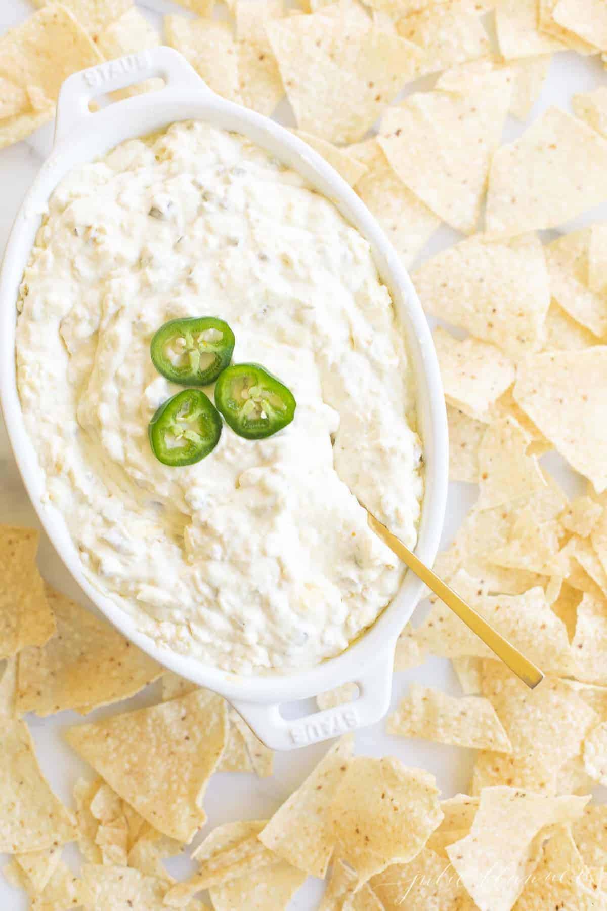 Creamy jalapeño dip in a white dish, chips surrounding it. 