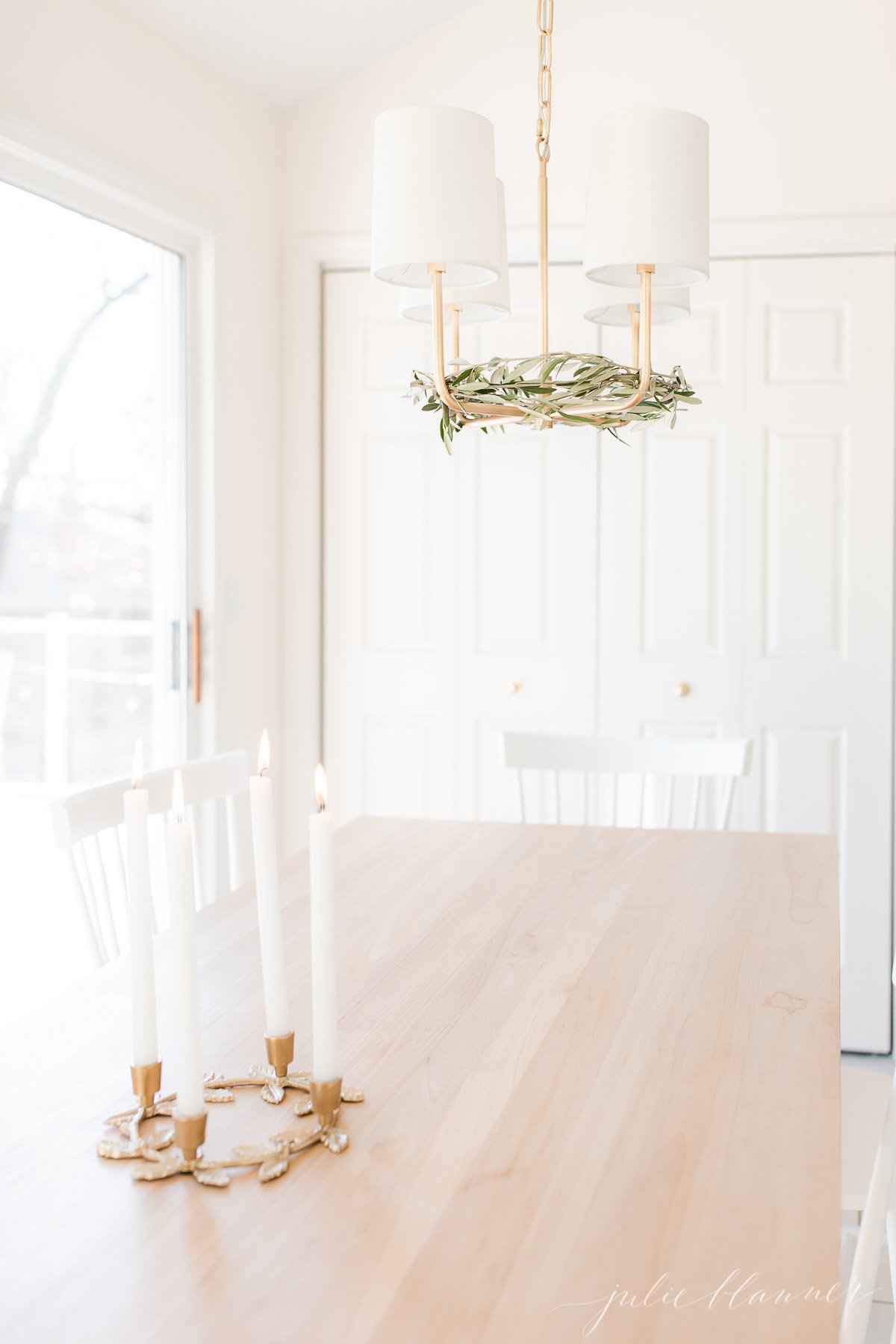 A white dining room table with white chairs and a gold laurel wreath candle holder centerpiece.