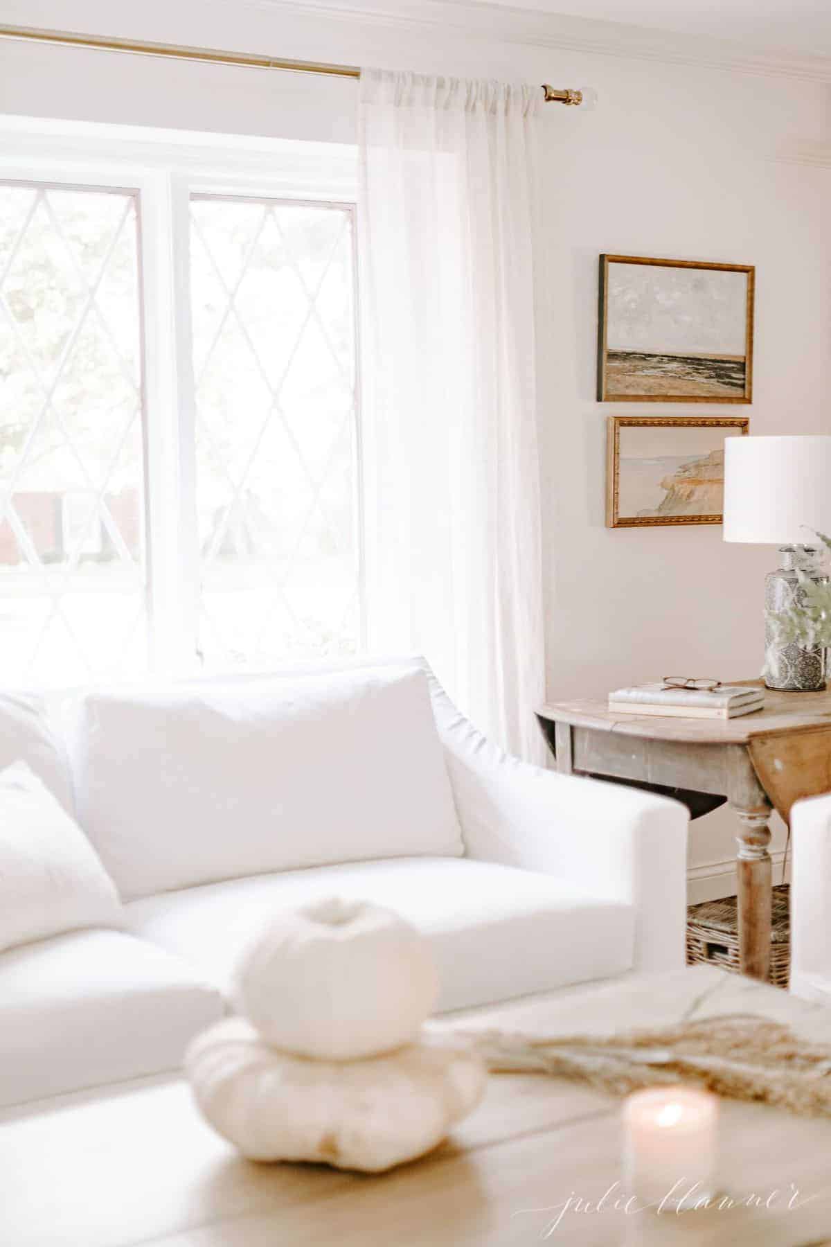 White sofa in living room, window behind. White pumpkin on coffee table in foreground. #falllivingroom