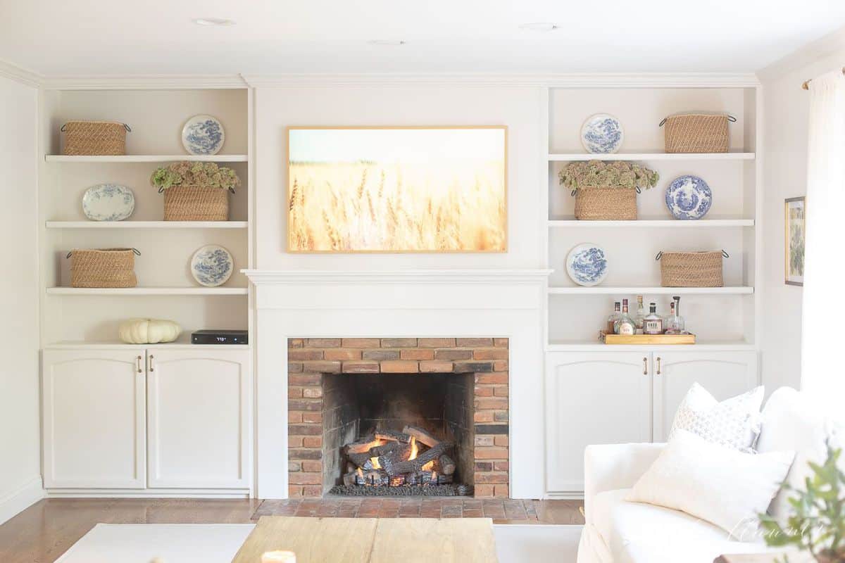 Living room fireplace burning with artwork above and bookshelves on each side. #falllivingroom