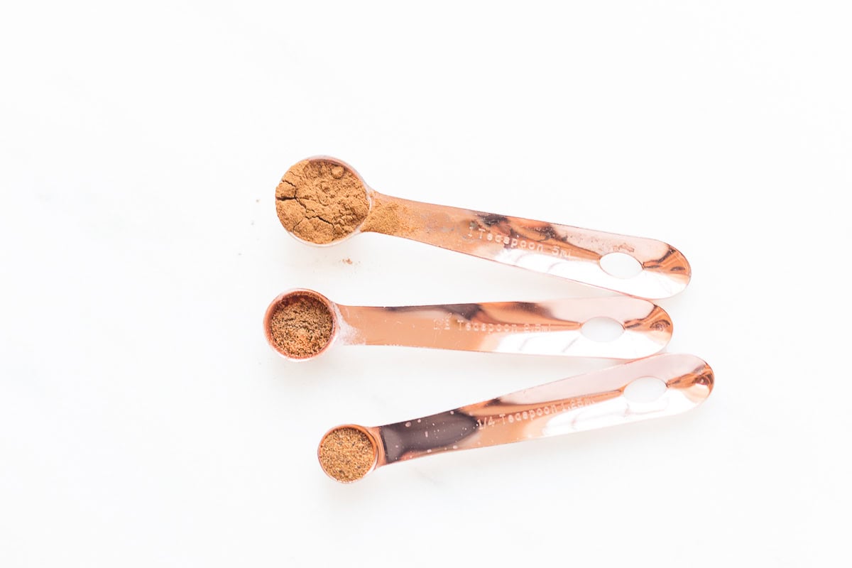 Three measuring spoons of varying sizes filled with ground cinnamon on a white background, accompanied by a handy measurement conversion chart.