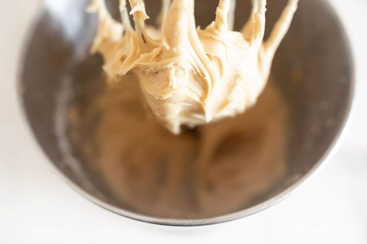 Peanut butter frosting in a stand mixer, whipping attachment is filled with frosting.