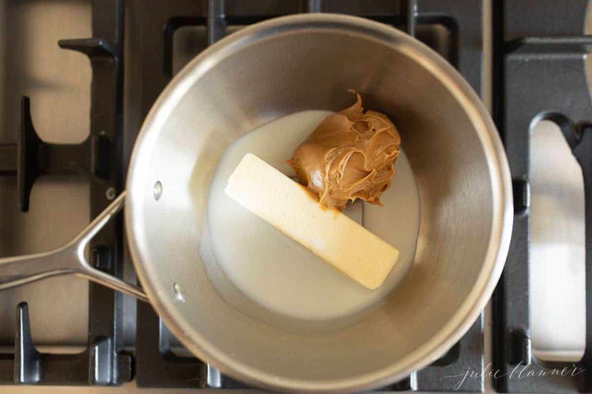 Stainless pan on a range, stick of butter and peanut butter inside.