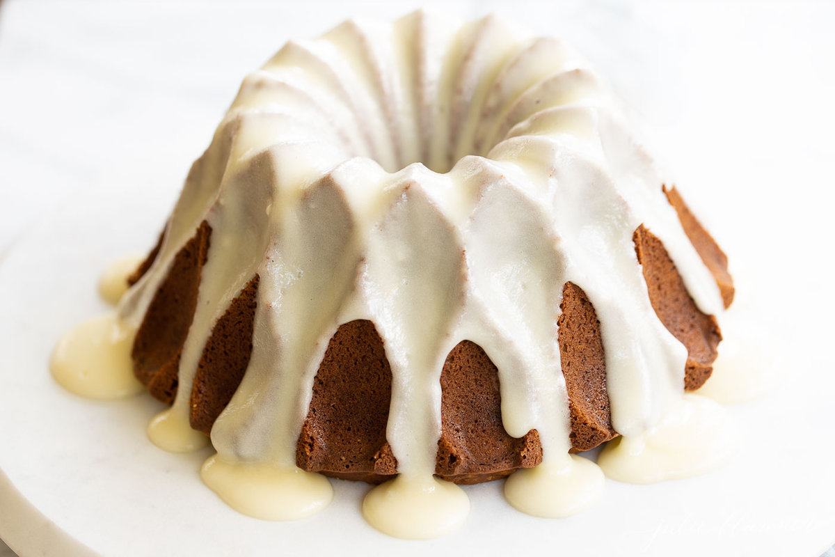 A frosted pumpkin bundt cake on a white marble surface.