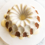A frosted pumpkin bundt cake on a white marble surface.