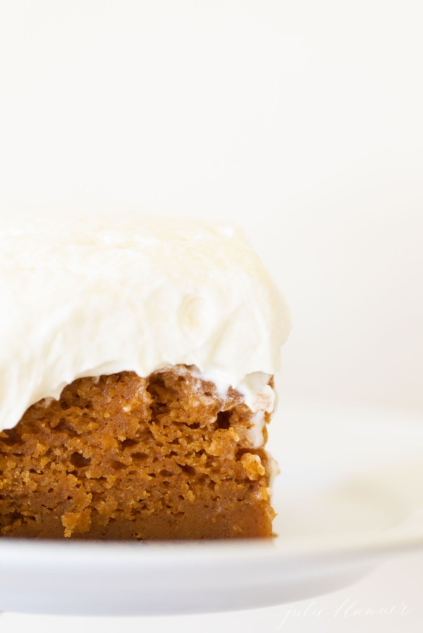 A slice of pumpkin cake with a thick layer of cream cheese frosting on a white plate.