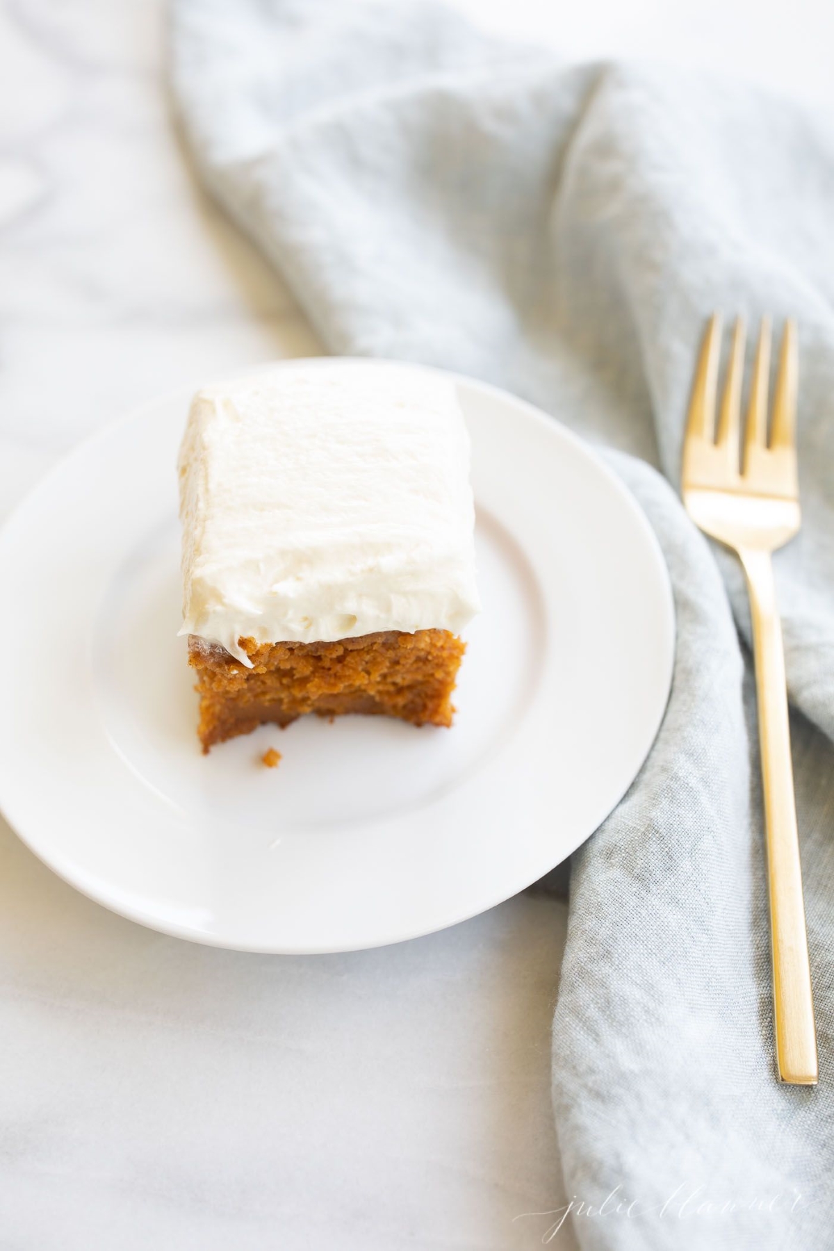 A slice of pumpkin cake with a thick layer of cream cheese frosting on a white plate.